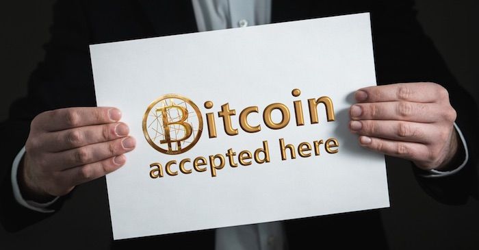Mann hält ein Schild "Bitcoin - Hier akzeptiert"
